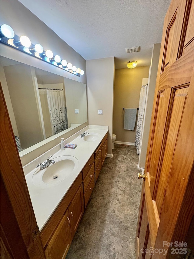 bathroom with toilet, a textured ceiling, double vanity, curtained shower, and baseboards