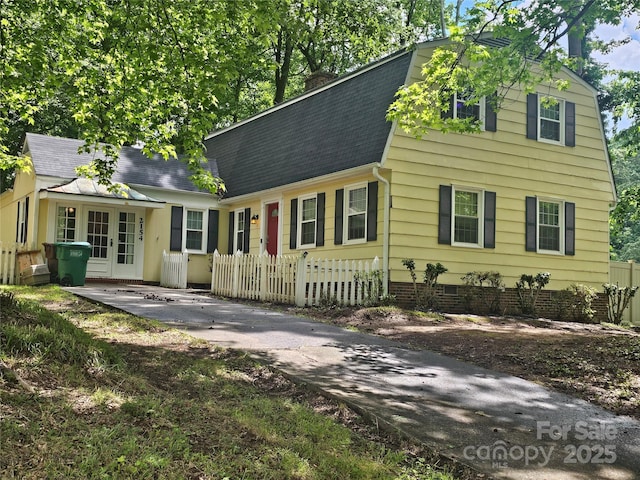 colonial inspired home with roof with shingles, a chimney, a fenced front yard, and a gambrel roof