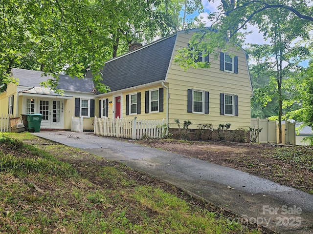 colonial inspired home with a chimney, a gambrel roof, roof with shingles, and a fenced front yard