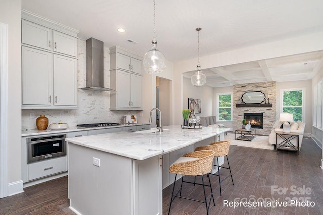 kitchen featuring wall chimney range hood, a sink, dark wood-style flooring, gas cooktop, and oven