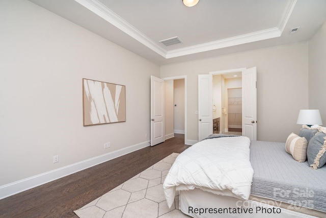 bedroom featuring a raised ceiling, wood finished floors, crown molding, and baseboards