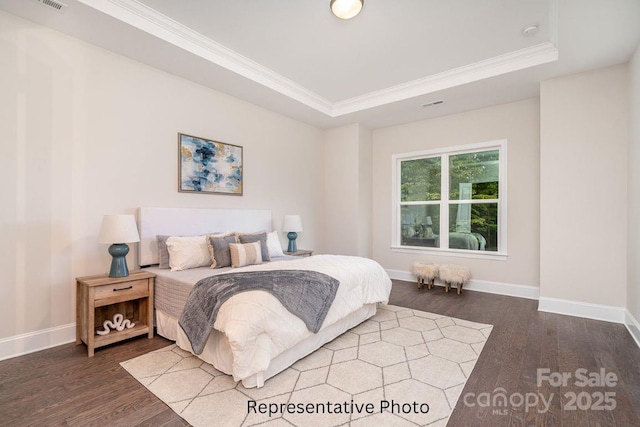 bedroom featuring wood finished floors, baseboards, a raised ceiling, and ornamental molding
