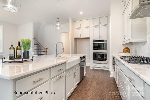 kitchen with a sink, appliances with stainless steel finishes, dark wood-type flooring, wall chimney range hood, and white cabinets