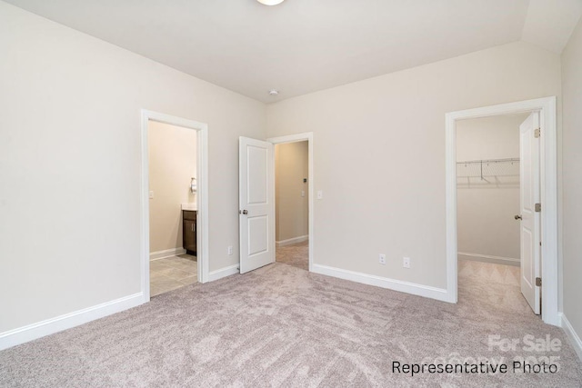 unfurnished bedroom featuring carpet, a walk in closet, a closet, and baseboards