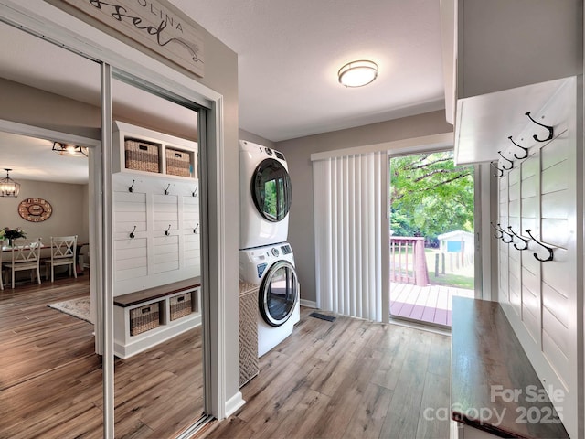 clothes washing area with stacked washer / drying machine, wood finished floors, a chandelier, and baseboards