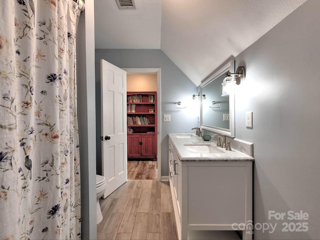 bathroom with wood finished floors, lofted ceiling, double vanity, toilet, and a shower with shower curtain