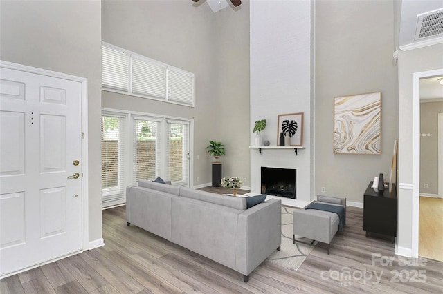 living room with a high ceiling, light wood-style flooring, baseboards, a fireplace, and ceiling fan
