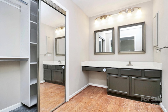 bathroom with wood finished floors, baseboards, and two vanities