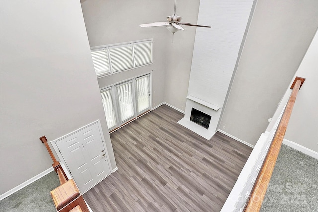 unfurnished living room featuring a towering ceiling, a ceiling fan, a fireplace with flush hearth, baseboards, and wood finished floors