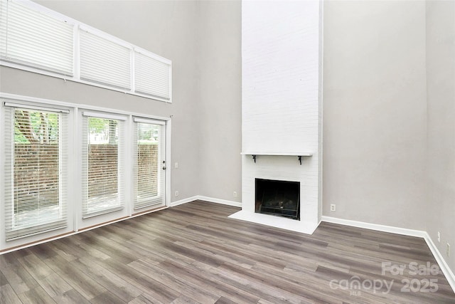 unfurnished living room featuring a towering ceiling, wood finished floors, healthy amount of natural light, a large fireplace, and baseboards