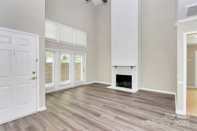 unfurnished living room featuring a towering ceiling, light wood-style flooring, a fireplace, and baseboards