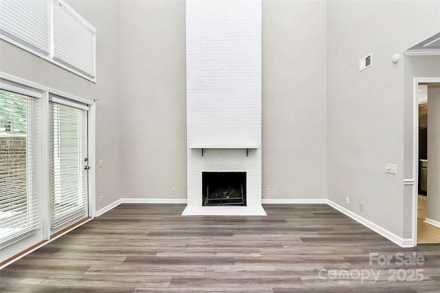 unfurnished living room featuring a high ceiling, wood finished floors, baseboards, and a fireplace