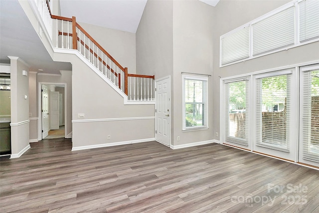 foyer entrance featuring a towering ceiling, wood finished floors, healthy amount of natural light, stairway, and baseboards