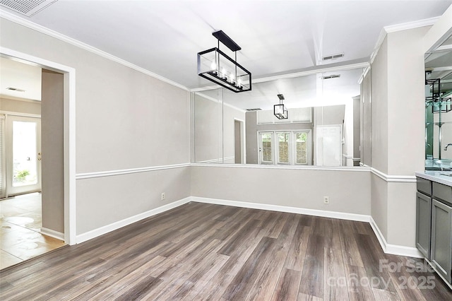 unfurnished dining area with wood finished floors, ornamental molding, baseboards, and a chandelier