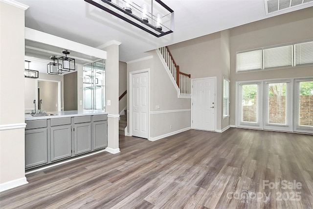 unfurnished living room featuring a chandelier, stairs, wood finished floors, and crown molding