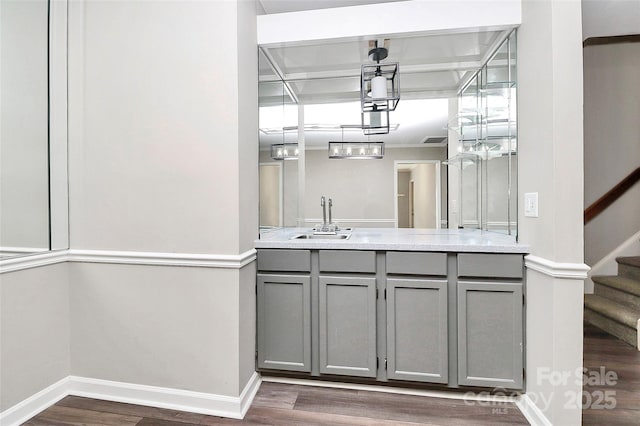 bar featuring a sink, dark wood-style floors, baseboards, stairs, and a chandelier
