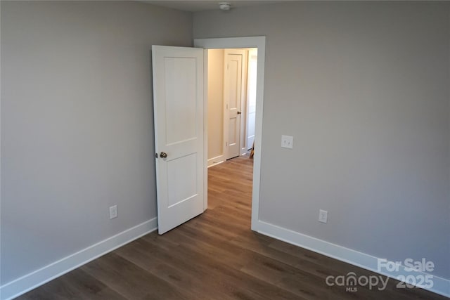 unfurnished room featuring baseboards and dark wood-style floors