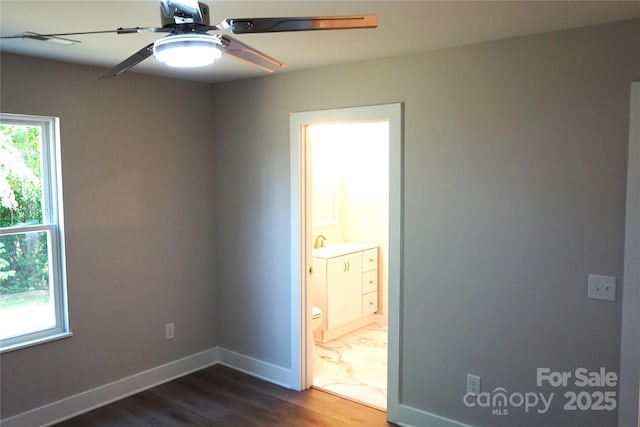empty room featuring dark wood-style floors, a ceiling fan, baseboards, and a sink