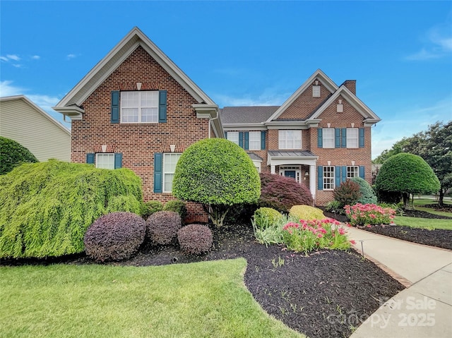 view of front of home featuring brick siding, a chimney, and a front lawn