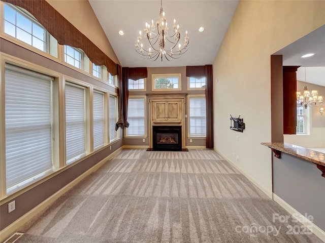 unfurnished living room featuring a chandelier, a fireplace with flush hearth, light colored carpet, high vaulted ceiling, and baseboards