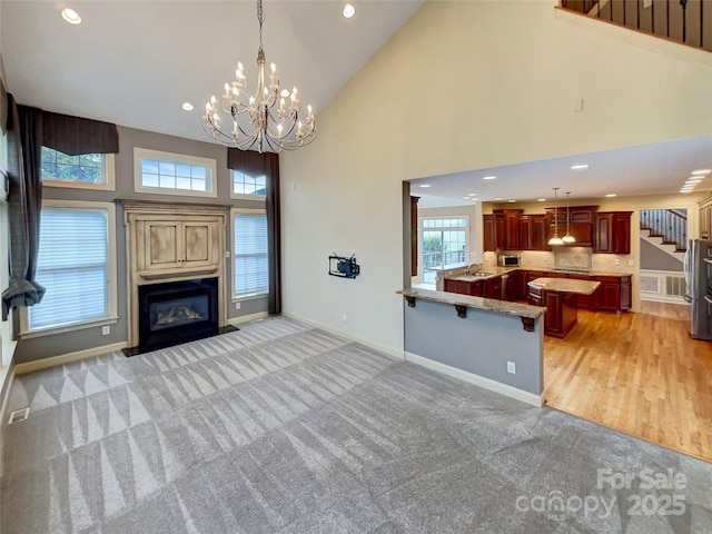 living area with light carpet, stairway, a glass covered fireplace, a chandelier, and high vaulted ceiling