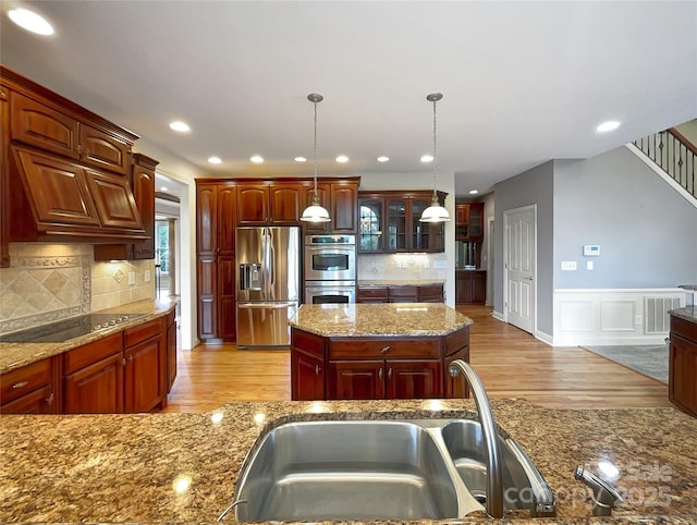 kitchen with stainless steel appliances, light wood-style floors, decorative light fixtures, decorative backsplash, and wainscoting