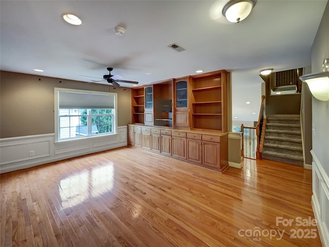 unfurnished living room with light wood-type flooring, a ceiling fan, wainscoting, stairs, and recessed lighting