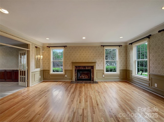 unfurnished living room featuring wallpapered walls, crown molding, a decorative wall, light wood-style flooring, and a premium fireplace