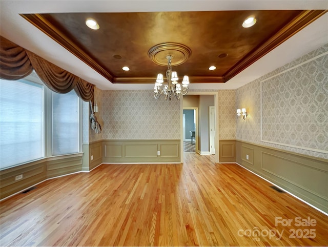 unfurnished dining area with a raised ceiling, a chandelier, a decorative wall, wallpapered walls, and light wood-style floors