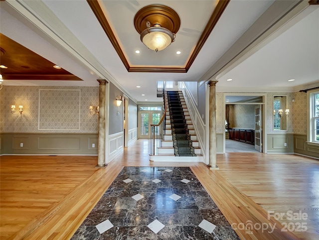 entryway with decorative columns, a decorative wall, a tray ceiling, crown molding, and healthy amount of natural light