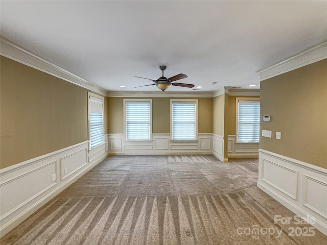 unfurnished room with crown molding, a decorative wall, wainscoting, ceiling fan, and light carpet