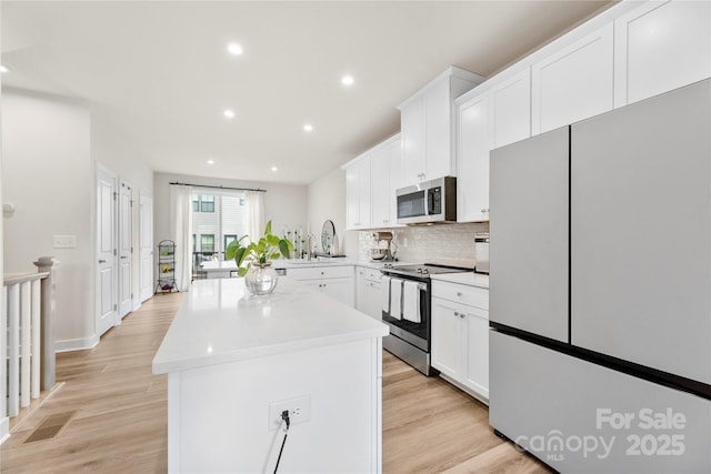 3748 Ellington St, Charlotte, NC 28211 - kitchen with appliances with stainless steel finishes, a center island, light wood finished floors, tasteful backsplash, and white cabinets