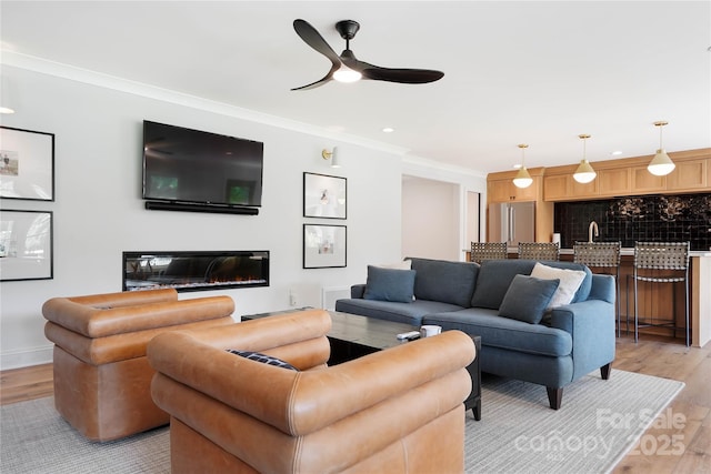 19946 River Falls Dr, Davidson, NC 28036 - living room with ceiling fan, light wood-style flooring, crown molding, a glass covered fireplace, and baseboards