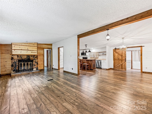 74 Saturn Ct, Clyde, NC 28721 - unfurnished living room featuring wooden walls, a textured ceiling, dark wood-style floors, a chandelier, and a stone fireplace