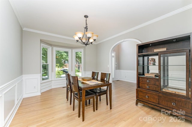 1147 Anduin Falls Dr, Charlotte, NC 28269 - dining room featuring a chandelier, arched walkways, light wood-style flooring, crown molding, and wainscoting