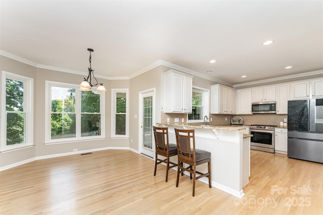 1147 Anduin Falls Dr, Charlotte, NC 28269 - kitchen with stainless steel appliances, light wood-style floors, a kitchen bar, decorative backsplash, and crown molding