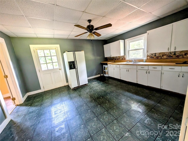 kitchen with white fridge with ice dispenser, a drop ceiling, a sink, plenty of natural light, and baseboards