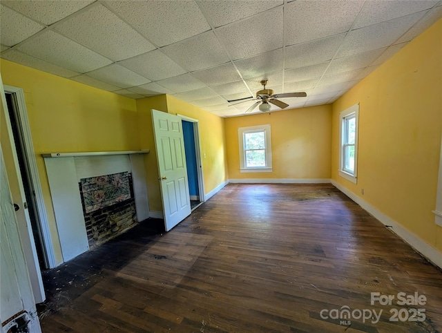 unfurnished living room featuring a drop ceiling, wood finished floors, a fireplace, a ceiling fan, and baseboards