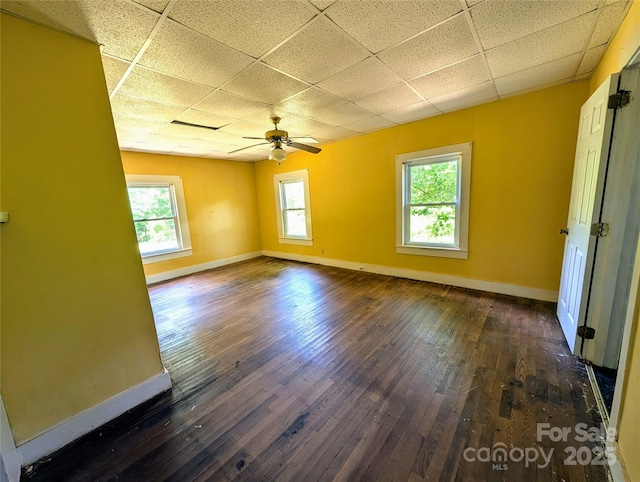 spare room featuring a drop ceiling, baseboards, ceiling fan, and dark wood-style floors