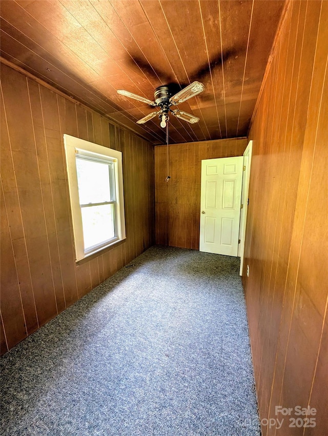 carpeted spare room with wood walls, a ceiling fan, and wood ceiling