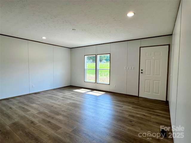 empty room featuring a textured ceiling, wood finished floors, recessed lighting, a decorative wall, and ornamental molding