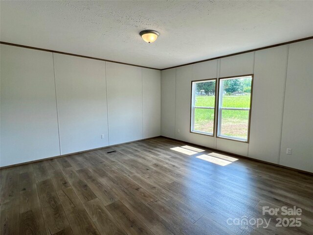 spare room featuring wood finished floors, a decorative wall, and a textured ceiling