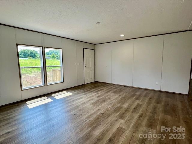 unfurnished room with a decorative wall, wood finished floors, a textured ceiling, and recessed lighting