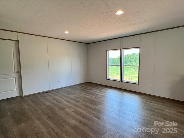 unfurnished room featuring a decorative wall, a textured ceiling, wood finished floors, and recessed lighting