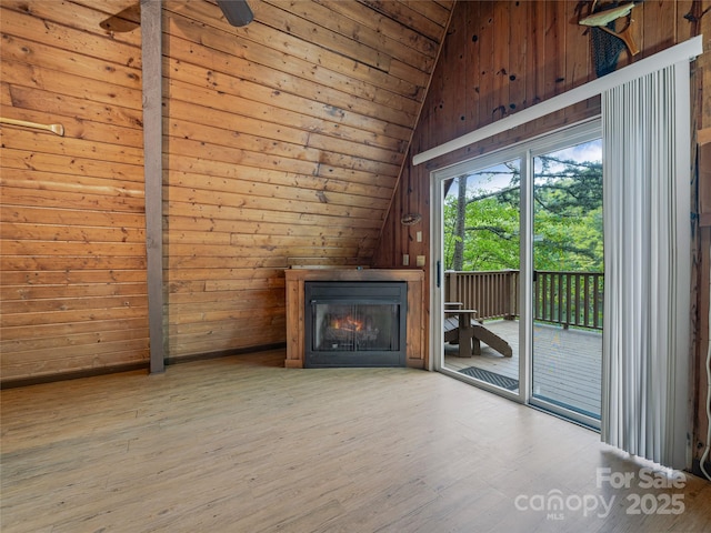 unfurnished living room with lofted ceiling, wooden ceiling, a warm lit fireplace, wood finished floors, and wooden walls