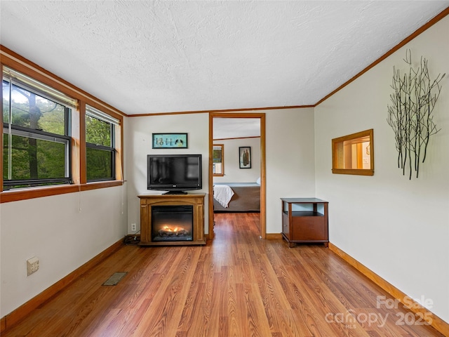 unfurnished living room with a textured ceiling, wood finished floors, ornamental molding, and baseboards