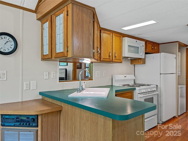 kitchen with white appliances, a sink, brown cabinets, light wood-type flooring, and a peninsula