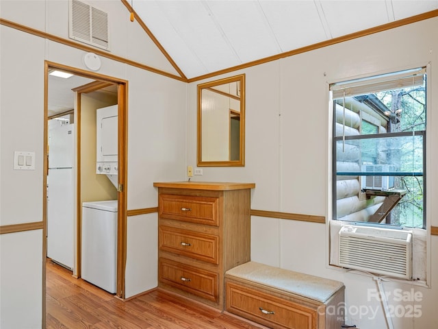 hallway with estacked washer and dryer, vaulted ceiling, light wood finished floors, healthy amount of natural light, and cooling unit