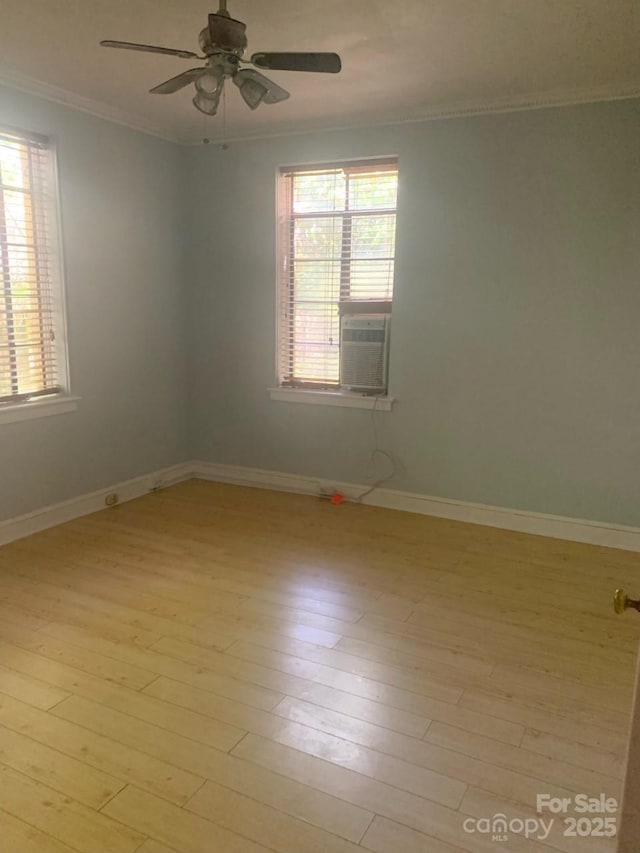spare room with ornamental molding, healthy amount of natural light, light wood-style flooring, a ceiling fan, and baseboards