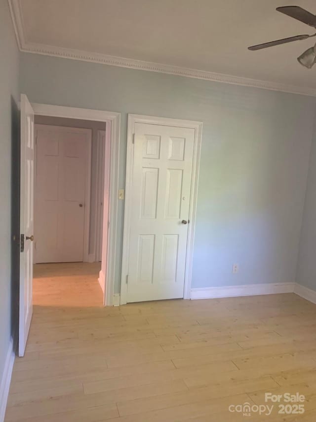 empty room with ornamental molding, ceiling fan, baseboards, and light wood-type flooring